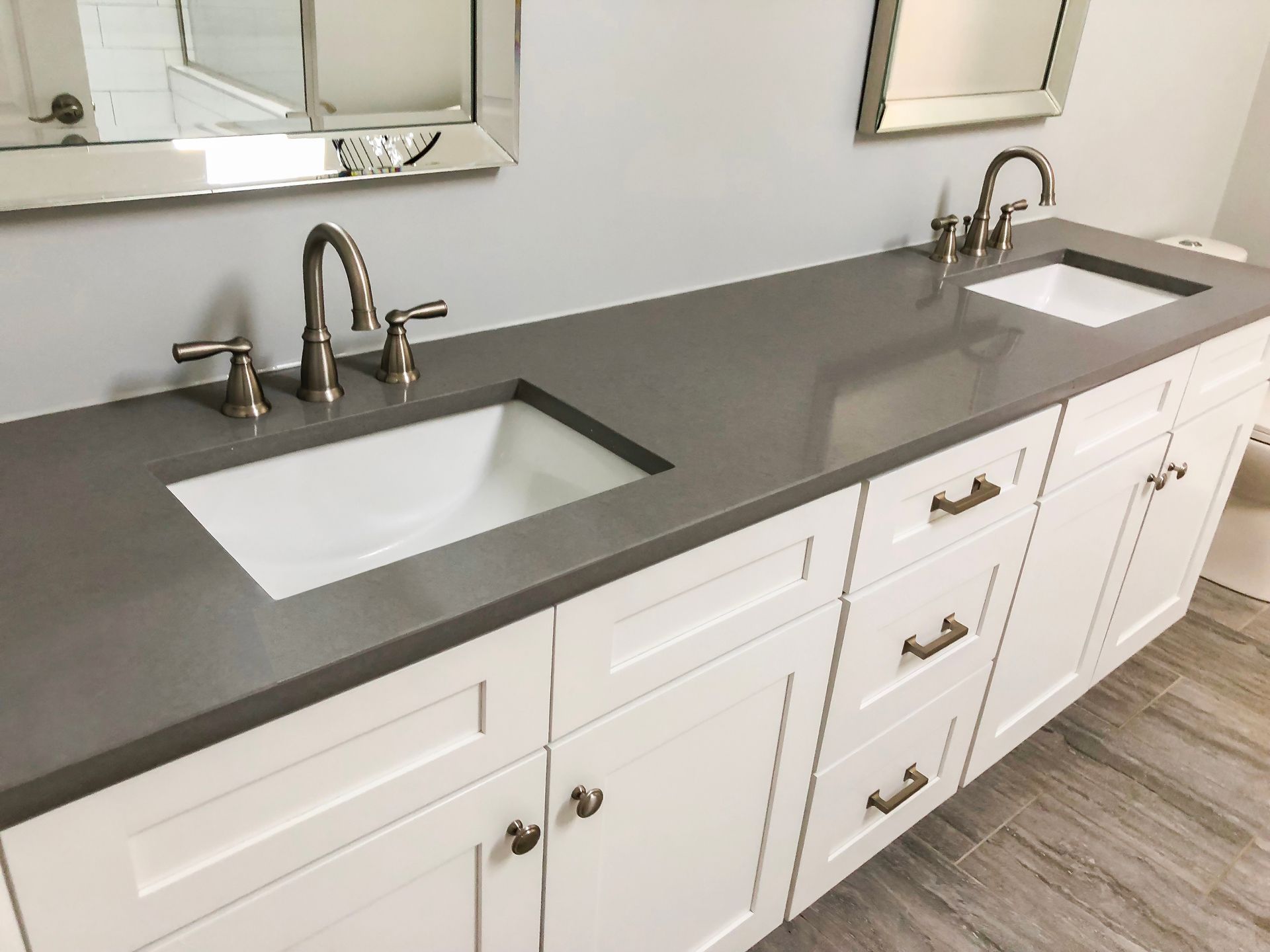 Modern bathroom vanity with double sinks, gray countertop, white cabinets, and chrome faucets