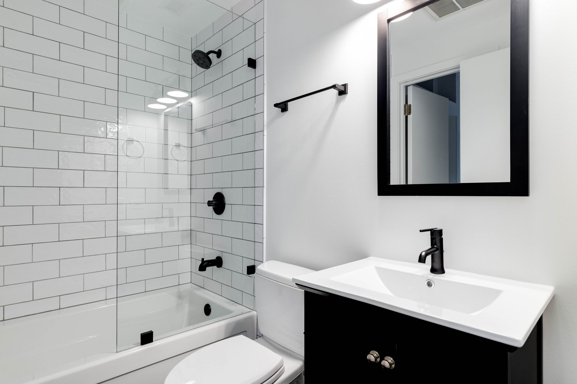 Modern white bathroom with glass shower, black fixtures, and a black vanity with mirror