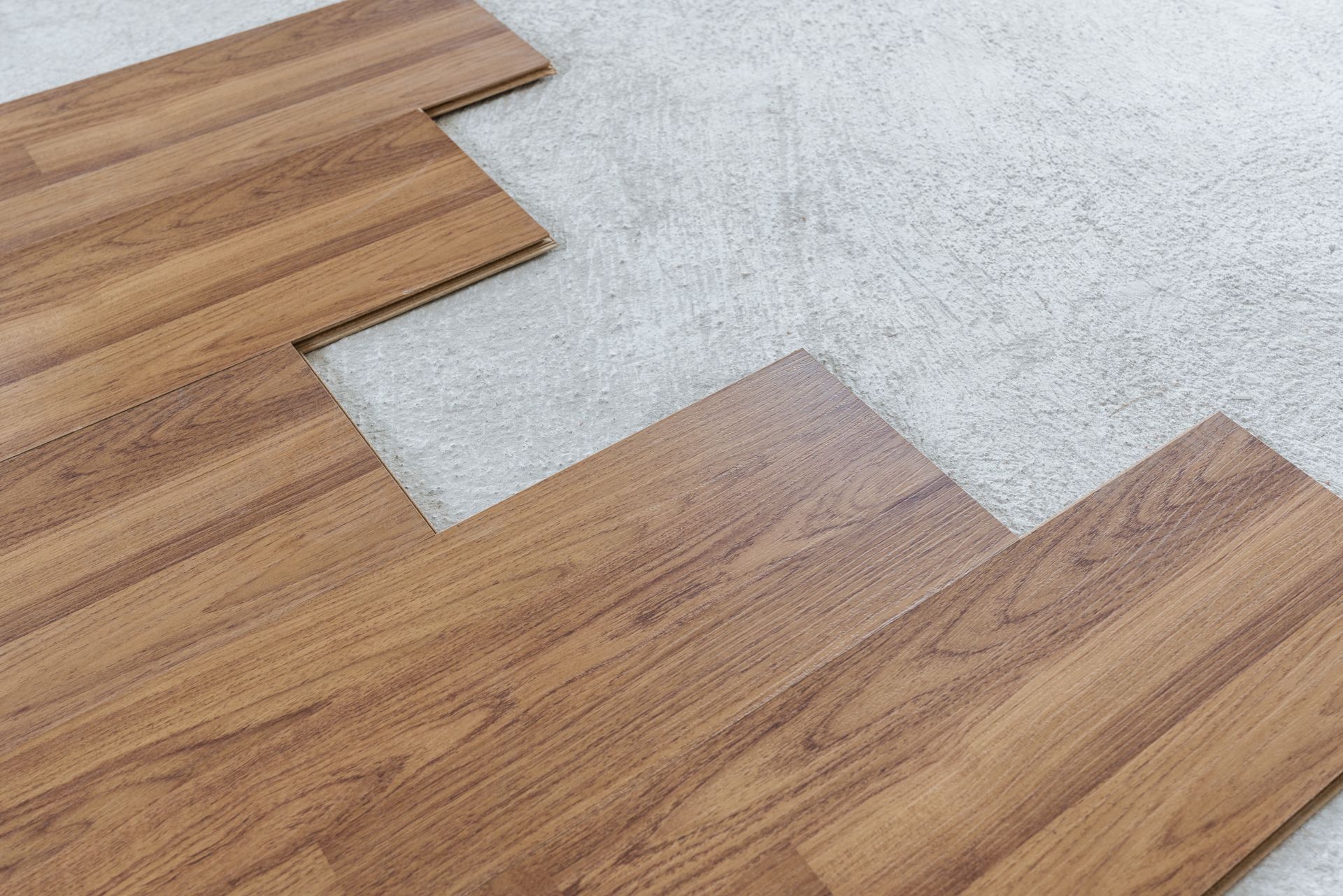 Wood-look laminate flooring being installed with interlocking planks over a gray underlayment.