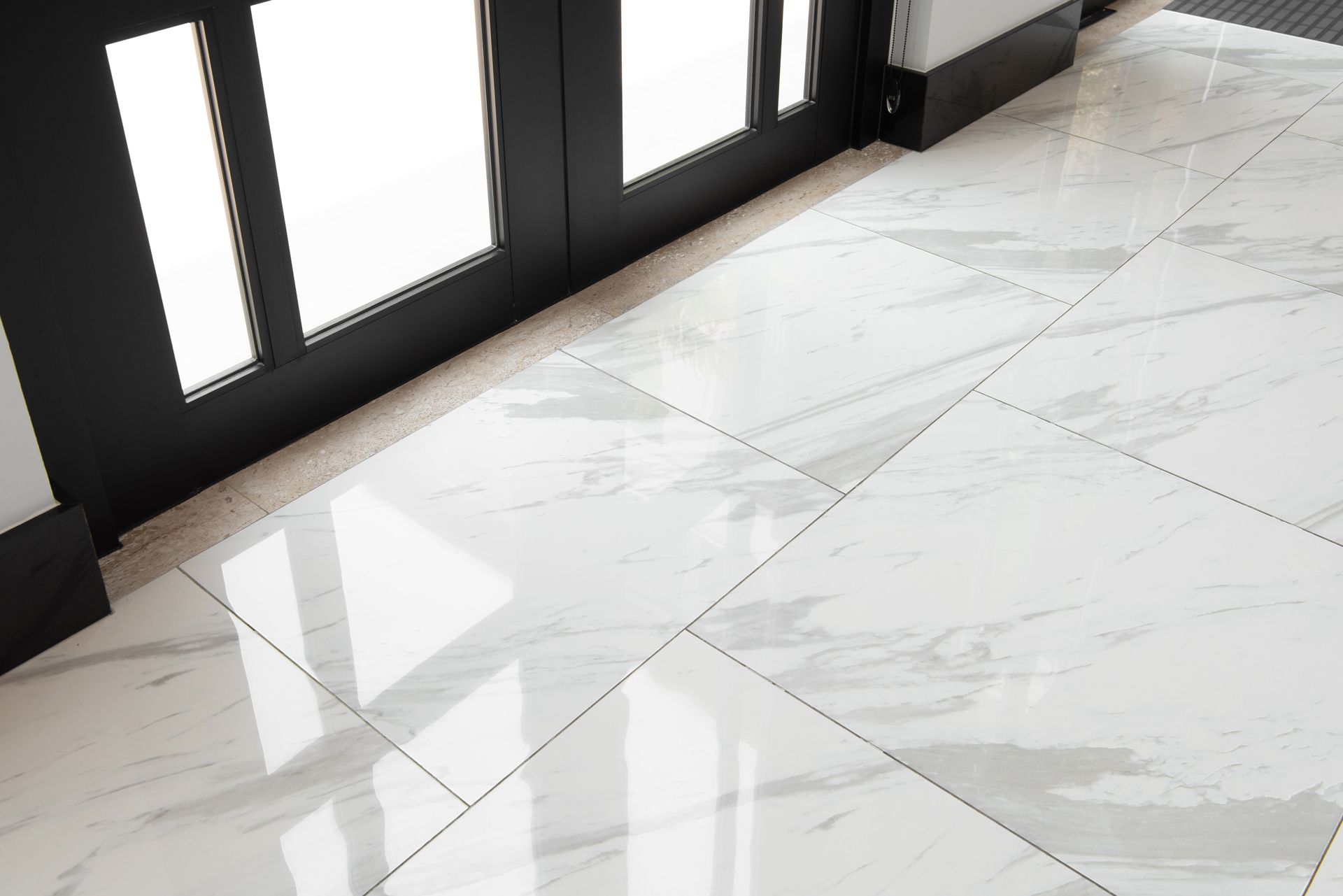 White marble tile floor beside black-framed glass doors with sunlight reflections