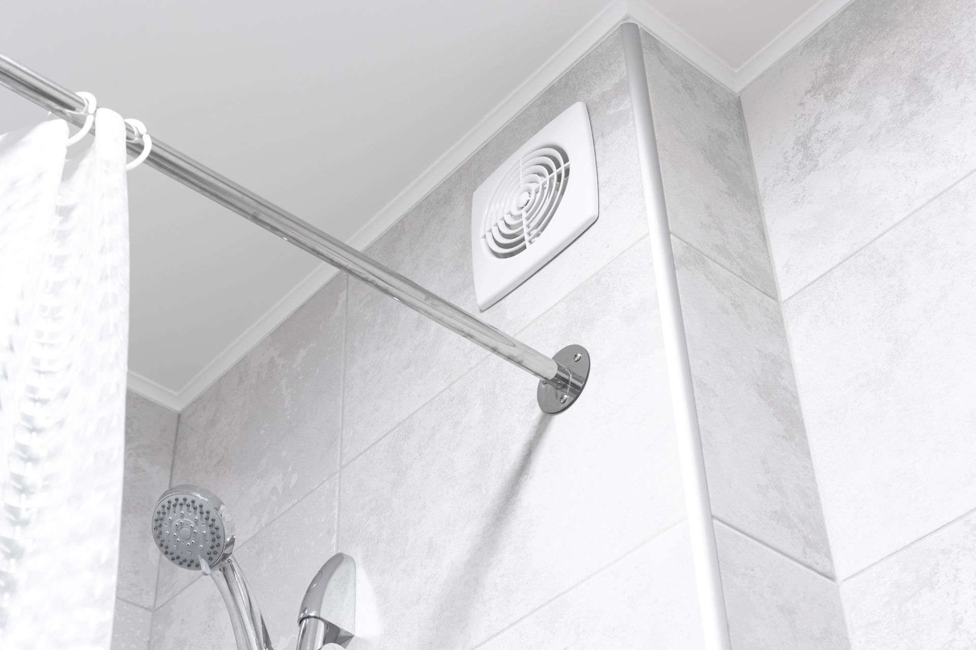 White-tiled bathroom shower with chrome showerhead, rod, and vent near the ceiling.