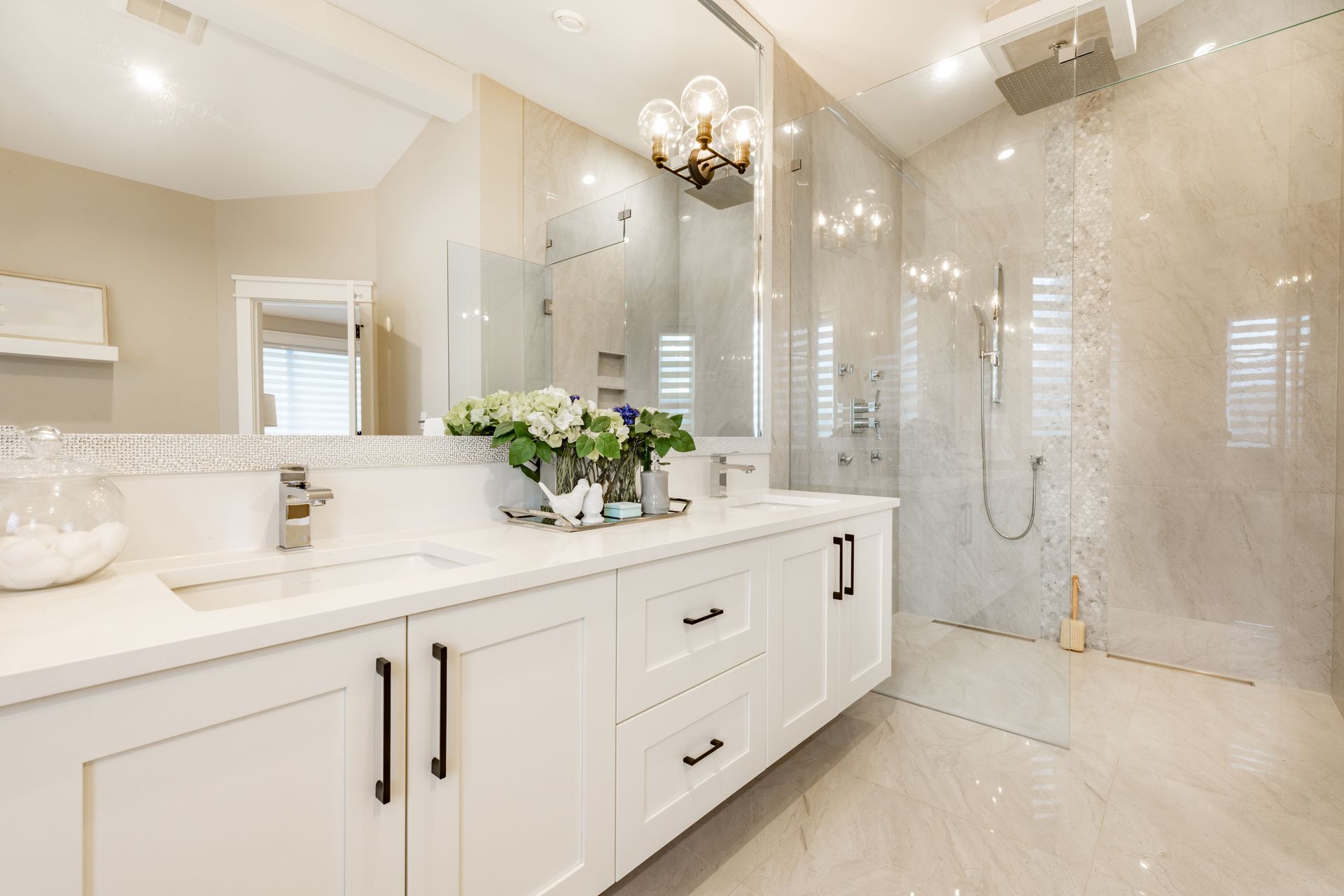 Bright modern bathroom with white vanity, marble shower, and chandelier lighting
