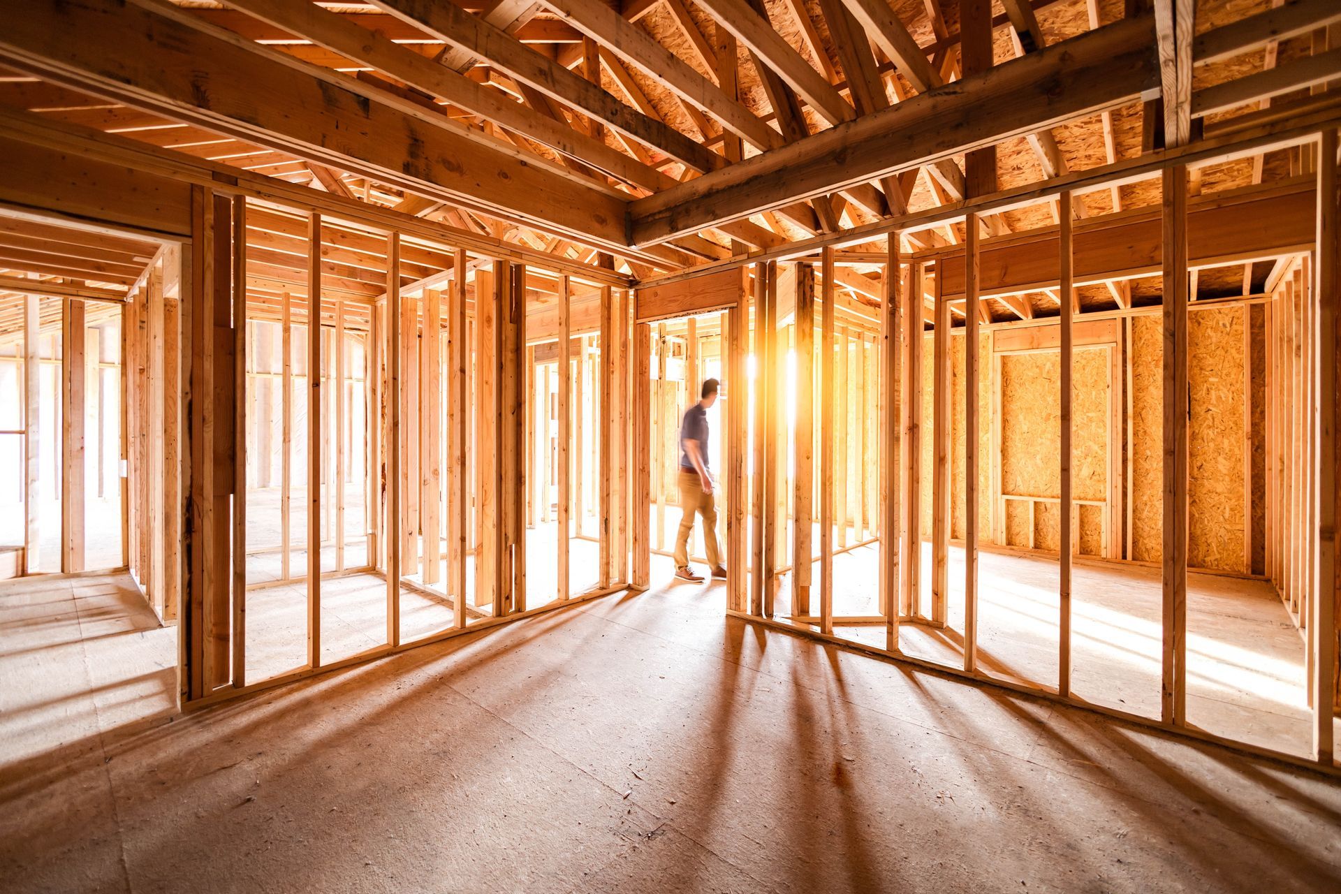 Framed house interior under construction with exposed wooden beams and a worker standing in the center.