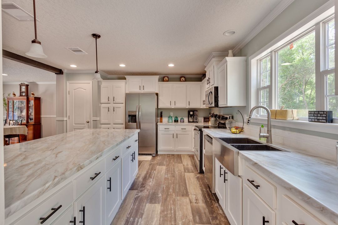Bright modern kitchen with white cabinets, marble counters, island, and large windows.