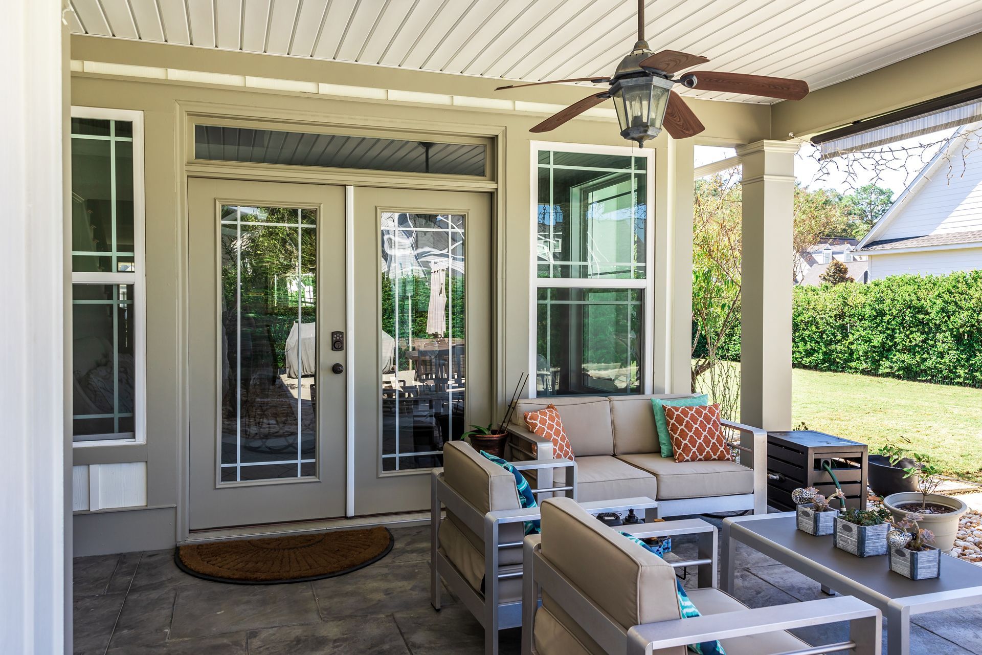 Covered patio with white outdoor sofa, chairs, and coffee table beside glass doors and green lawn