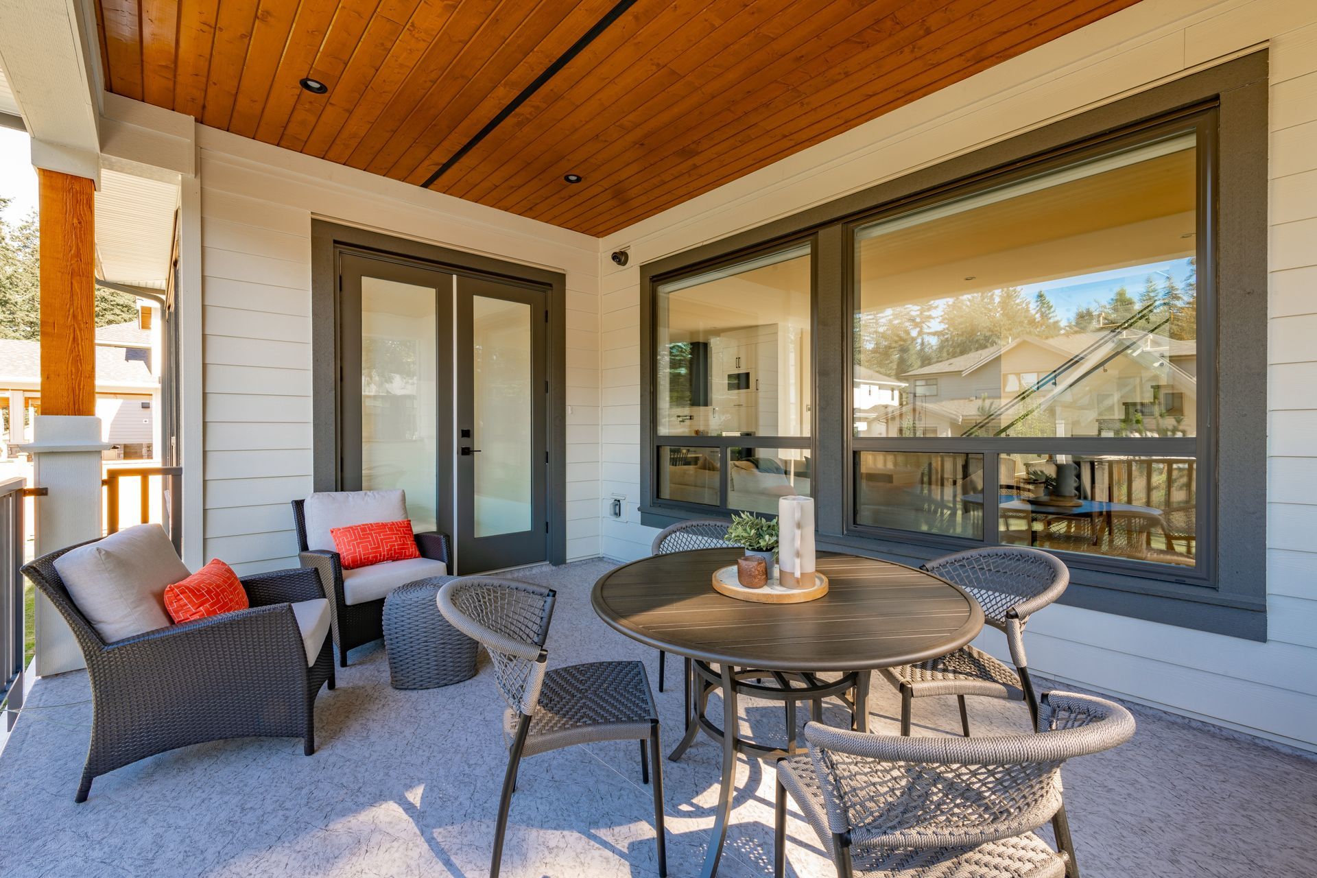 Covered patio with wicker seating, round table, and large windows under a wood-paneled ceiling.