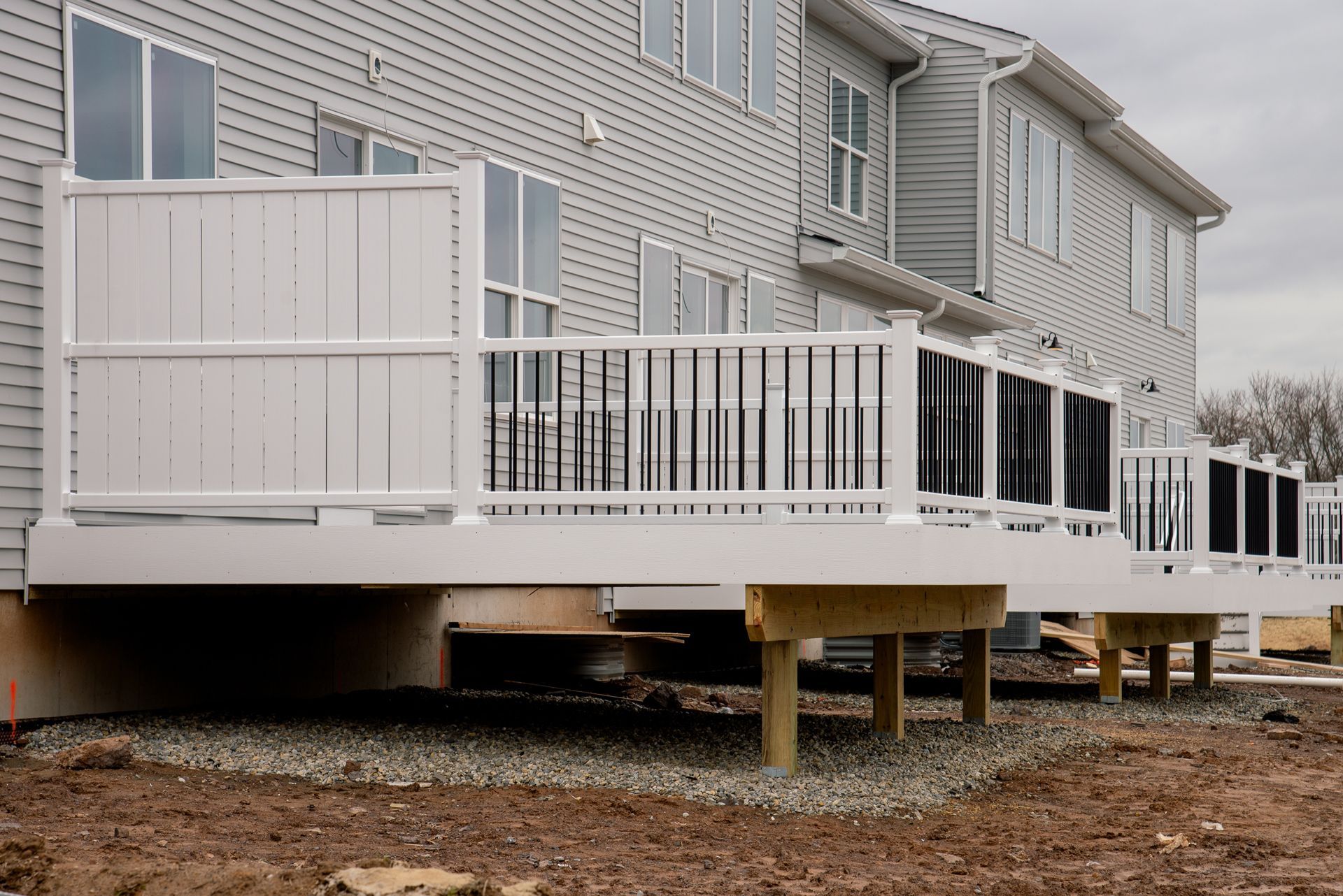 Raised white deck attached to a house, with railings and stairs over a gravel yard