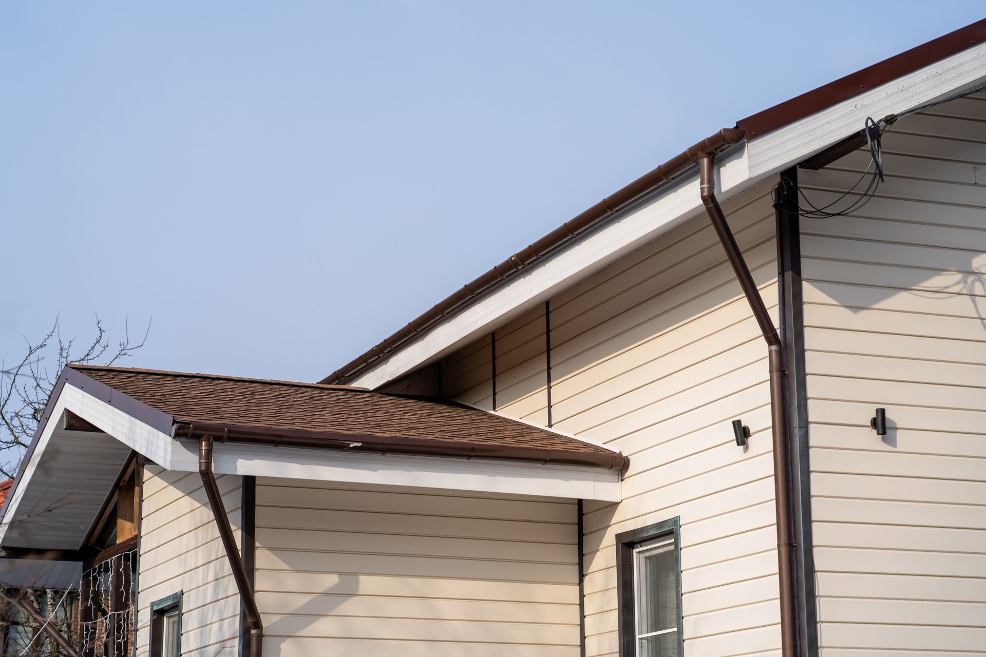 Exterior of a beige house with brown roof and white trim against a clear blue sky