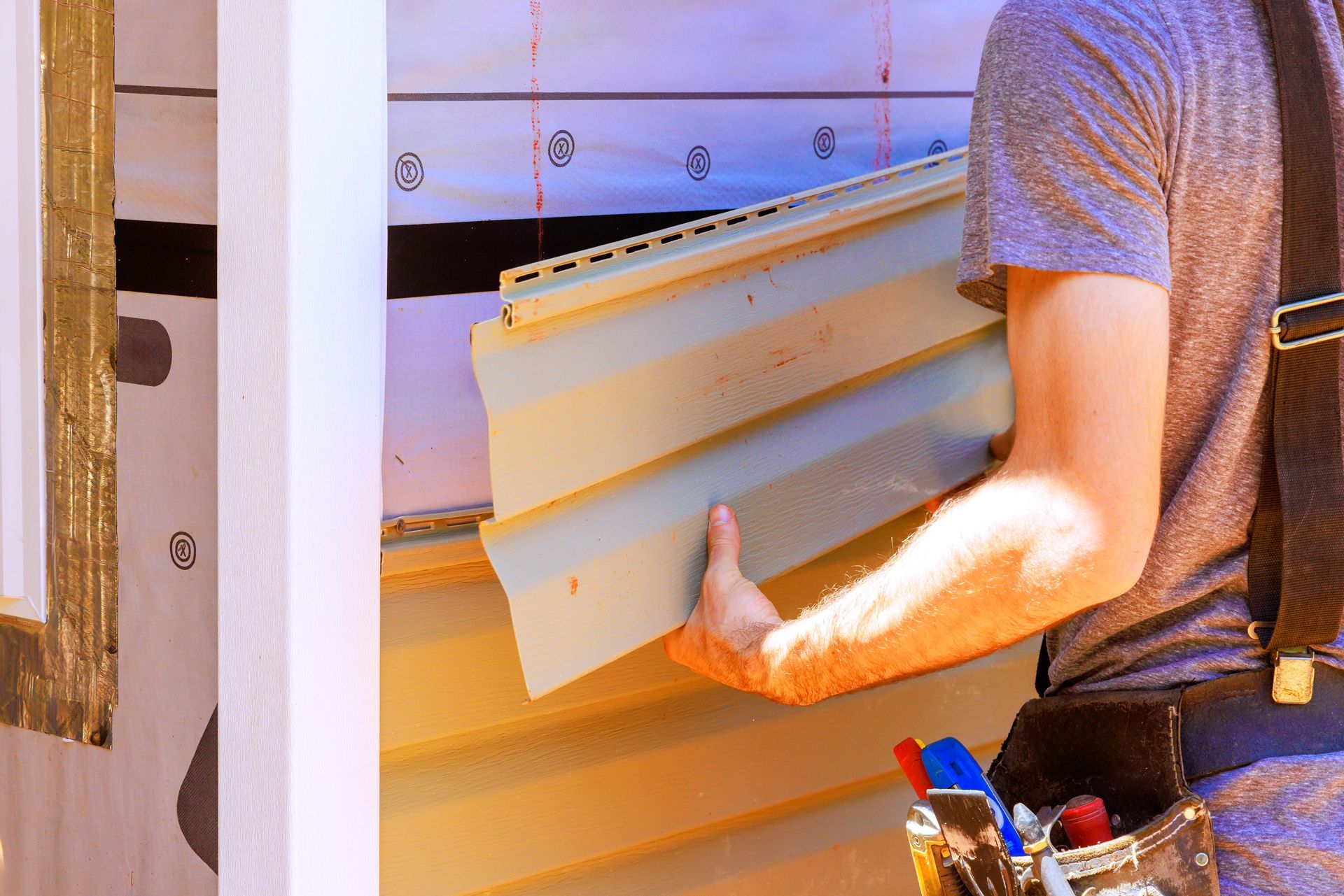 Worker installing white siding on a house exterior