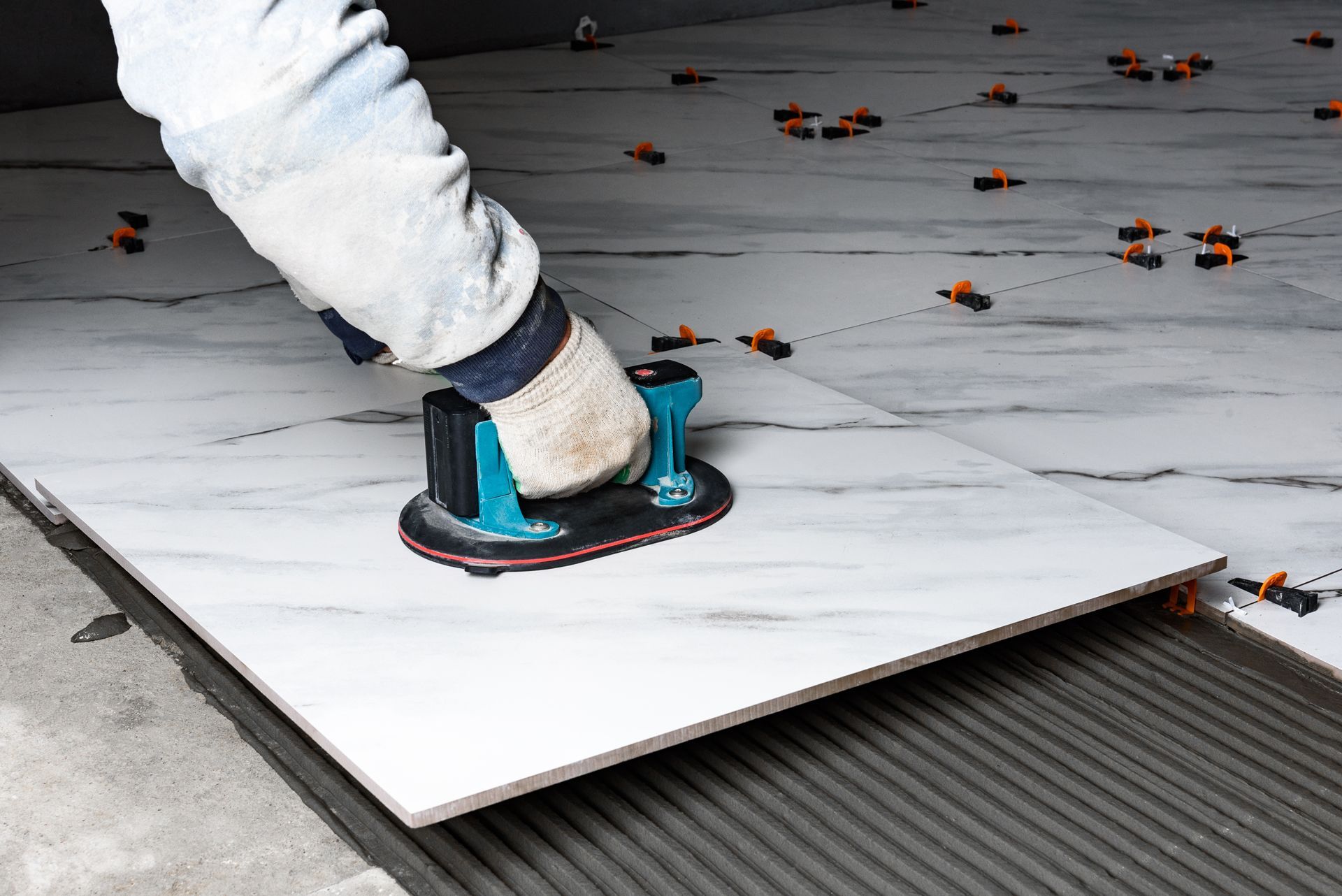 Worker using a blue tile cutter on large white floor tiles during installation