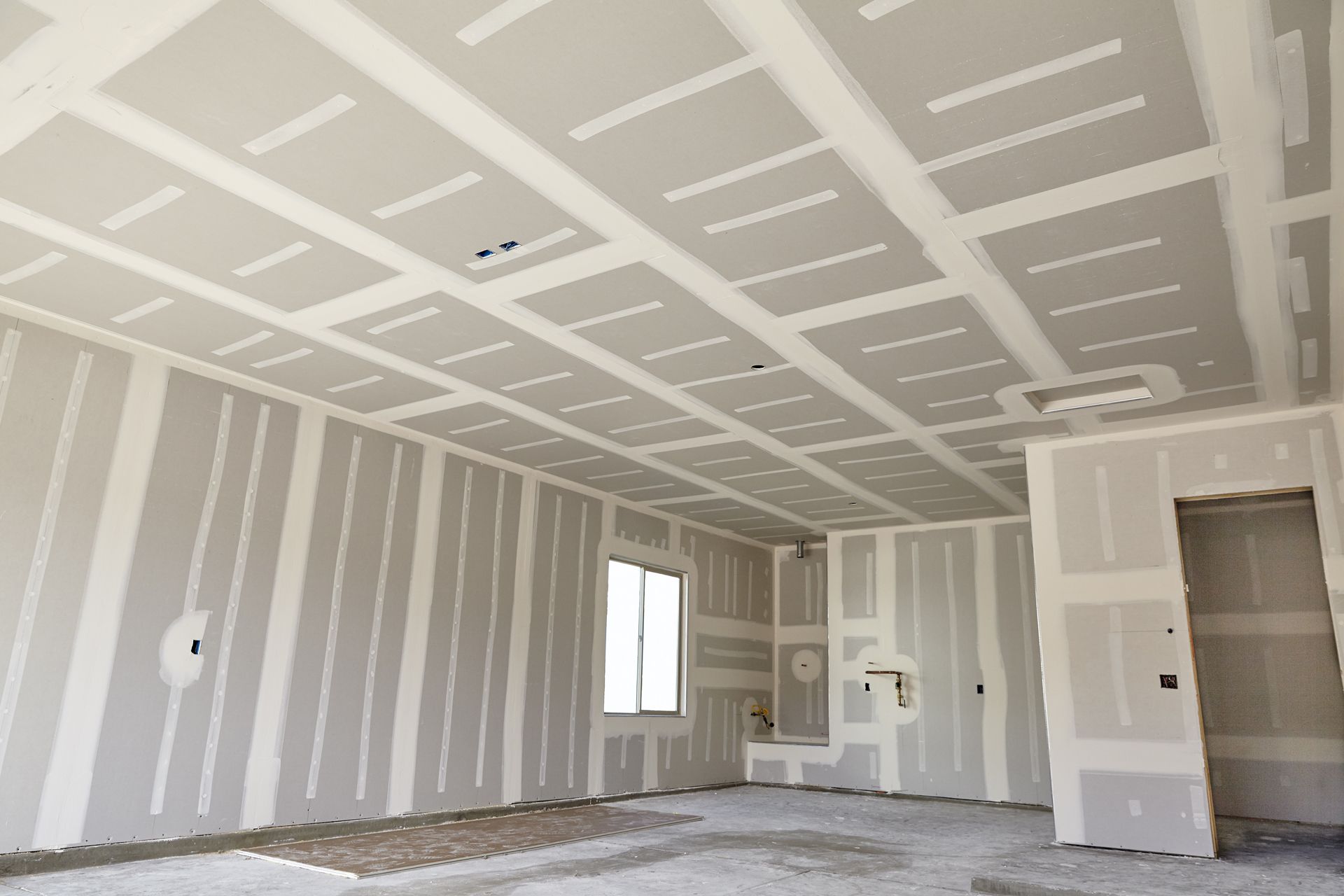 Empty room under construction with drywall, taped seams, a window, and a doorway