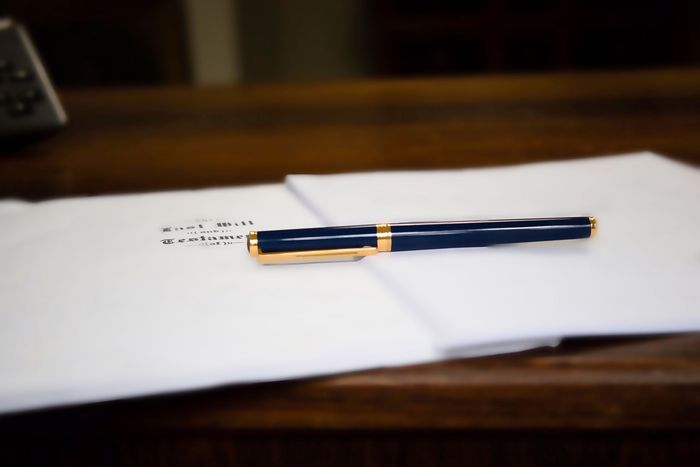 Penna stilografica su un foglio di carta bianco con testo scritto a mano, appoggiata su una scrivania di legno.