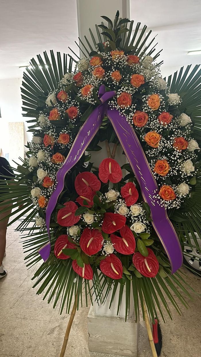 Composizione floreale con rose arancioni, anthurium rossi e nastro viola.