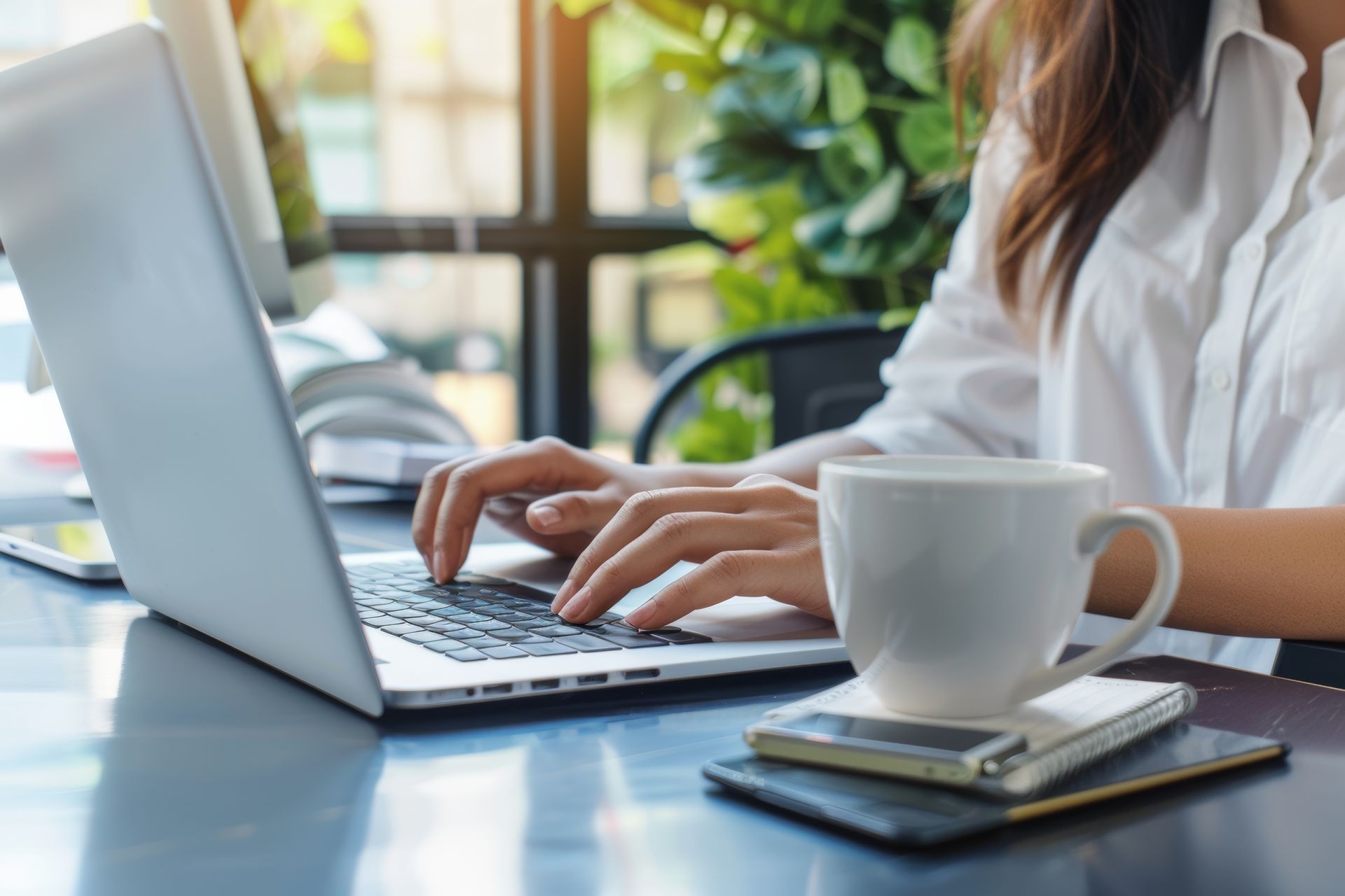 A woman is typing on a laptop computer while sitting at a table with a cup of coffee.