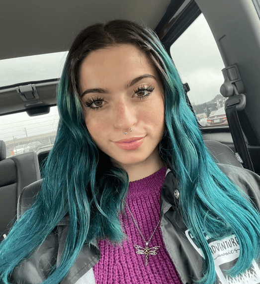 Woman smiling, wearing a beige sweater and colorful necklace, against a light blue background.