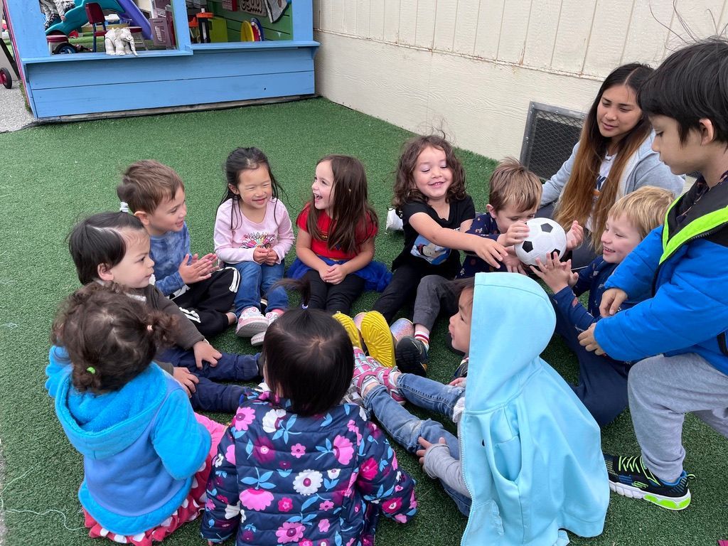 Three babies playing with colorful blocks, smiling and sitting on a floor mat.
