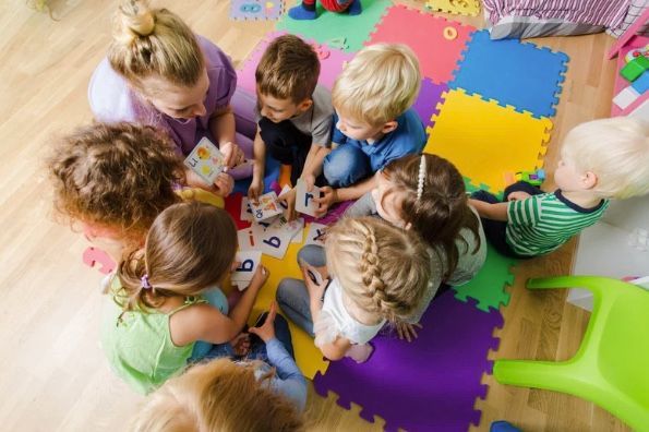 Children and adult seated on floor playing with colorful cards.
