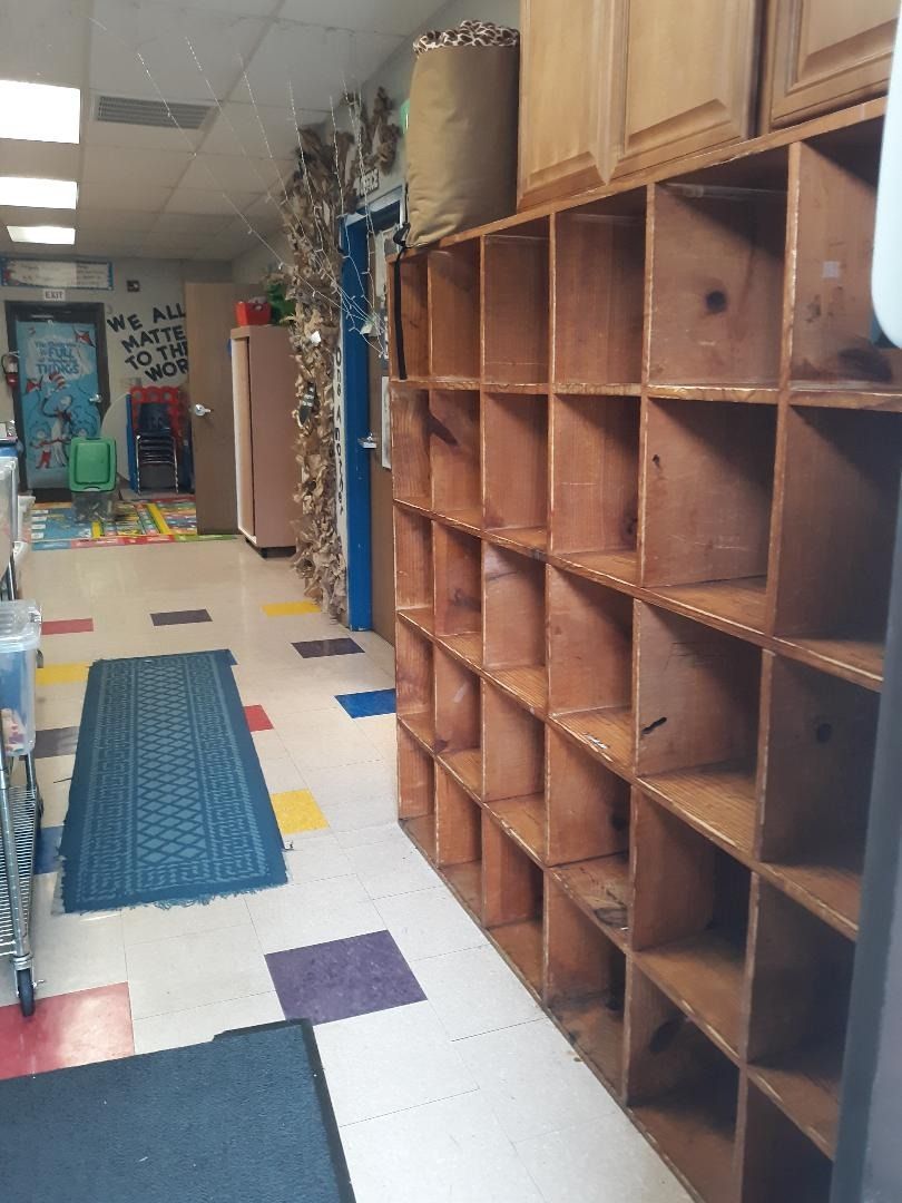 Empty wooden cubby shelves line a hallway with colorful floor tiles.