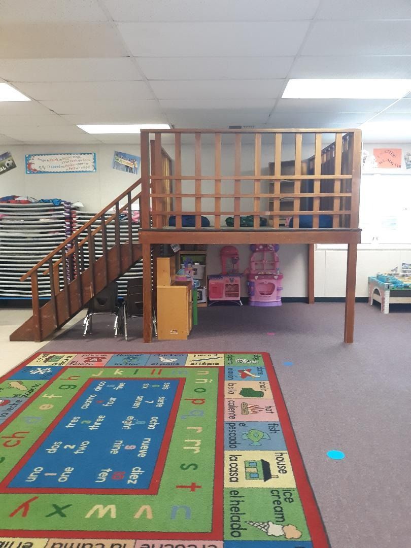 Indoor playspace with a wooden loft, stairs, and a rug.