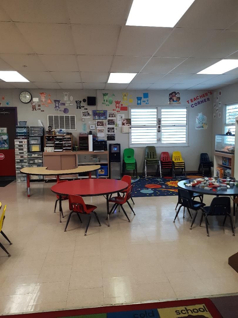 A brightly lit preschool classroom with tables, chairs, and colorful decorations on the walls.