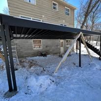 Black deck structure over a snowy yard next to a brick building.