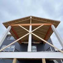 Wooden pergola with angled roof beams, supported by white posts, attached to a house.