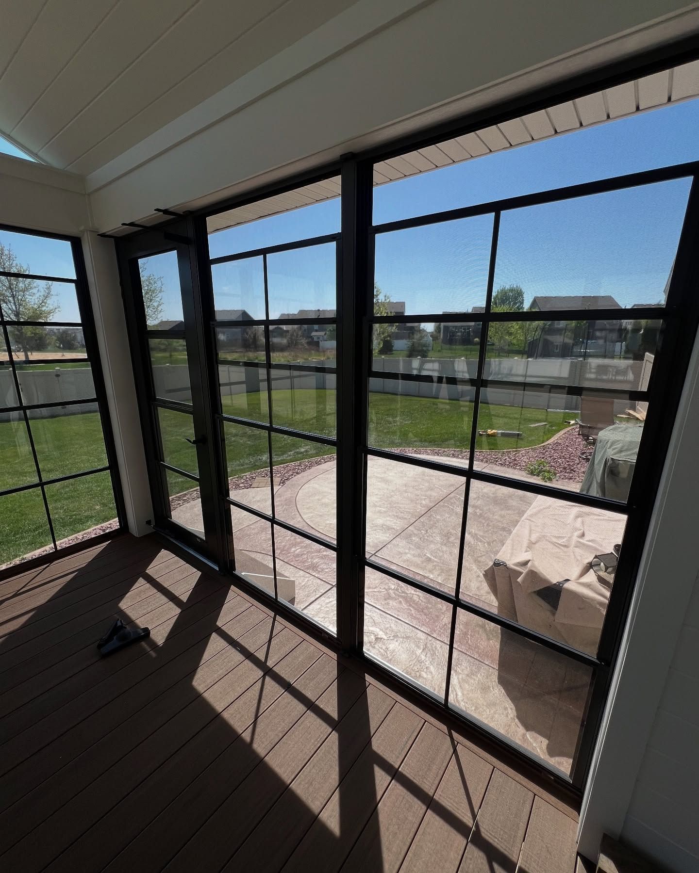 Sunroom with black-framed windows overlooking a patio and yard; brown deck flooring.