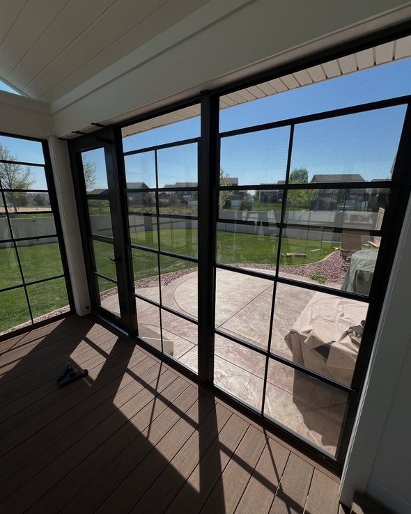 Sunroom with black-framed windows overlooking a patio and yard; brown deck flooring.