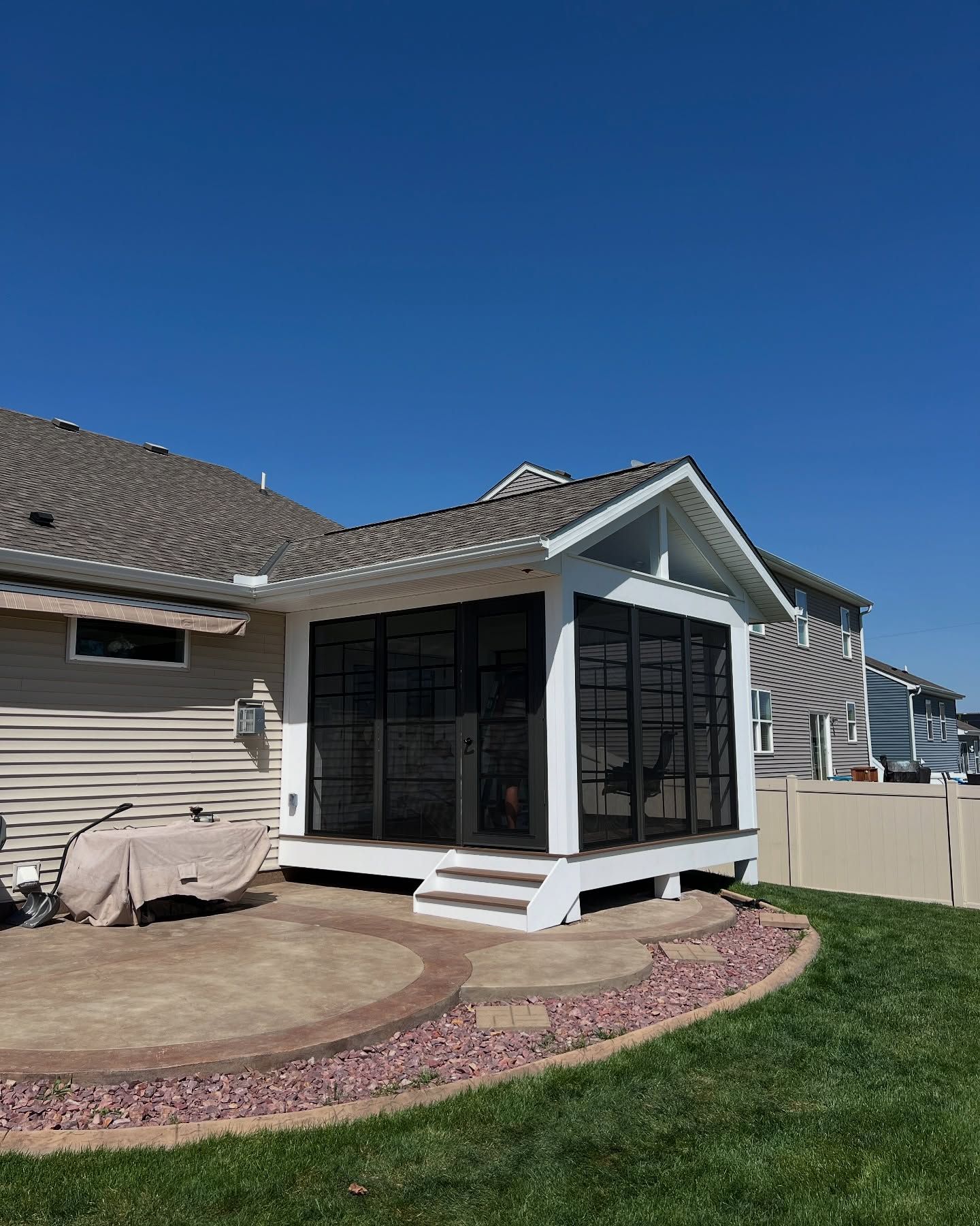 Screened porch attached to a tan house with a concrete patio and green lawn on a sunny day.