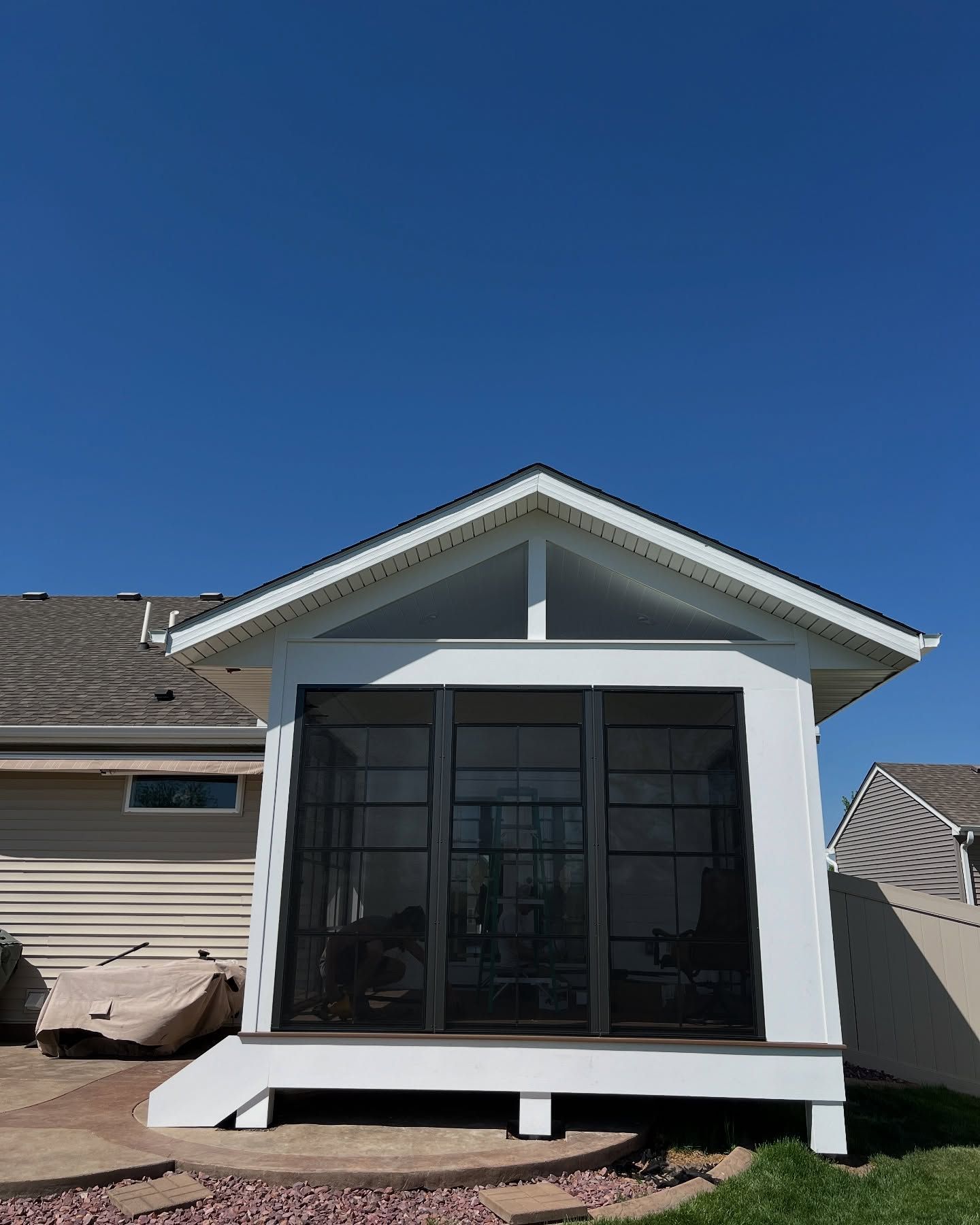 White screened porch with a gabled roof on a sunny day.