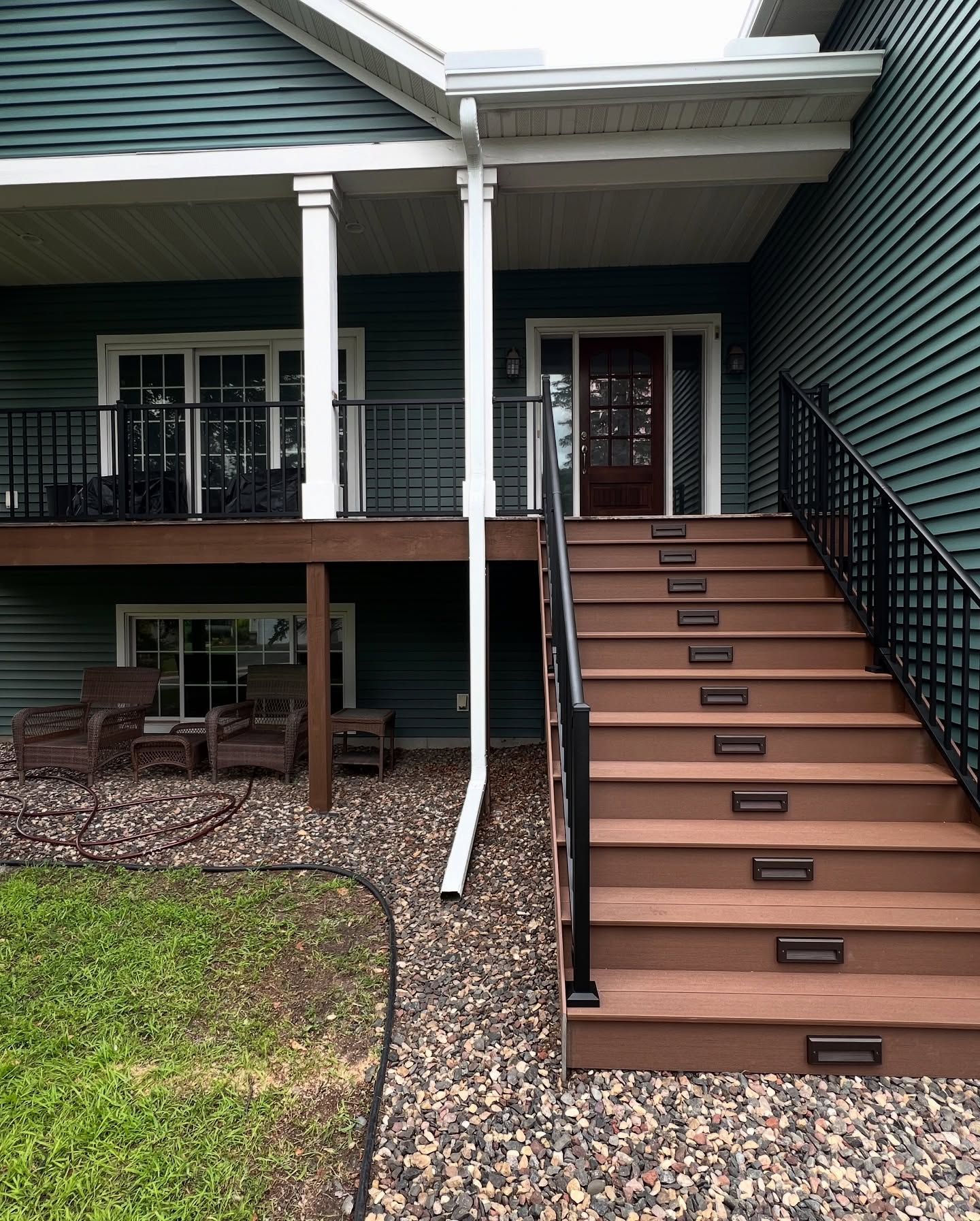 Green house with brown stairs, railing, and a covered porch.