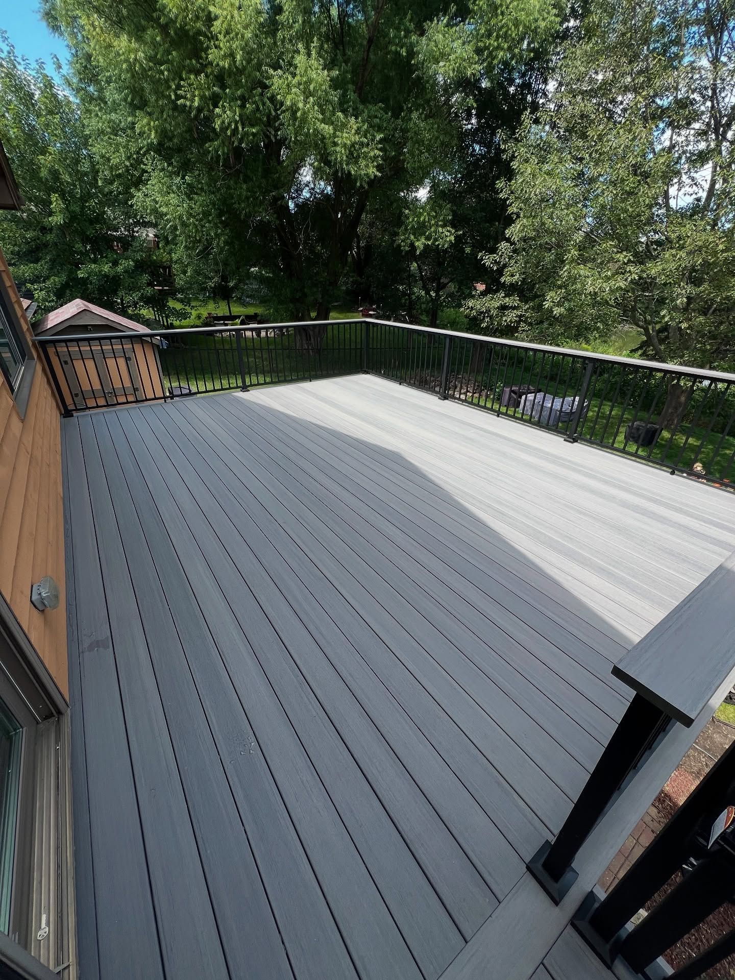 Gray composite deck with black railing and lush trees in the background.