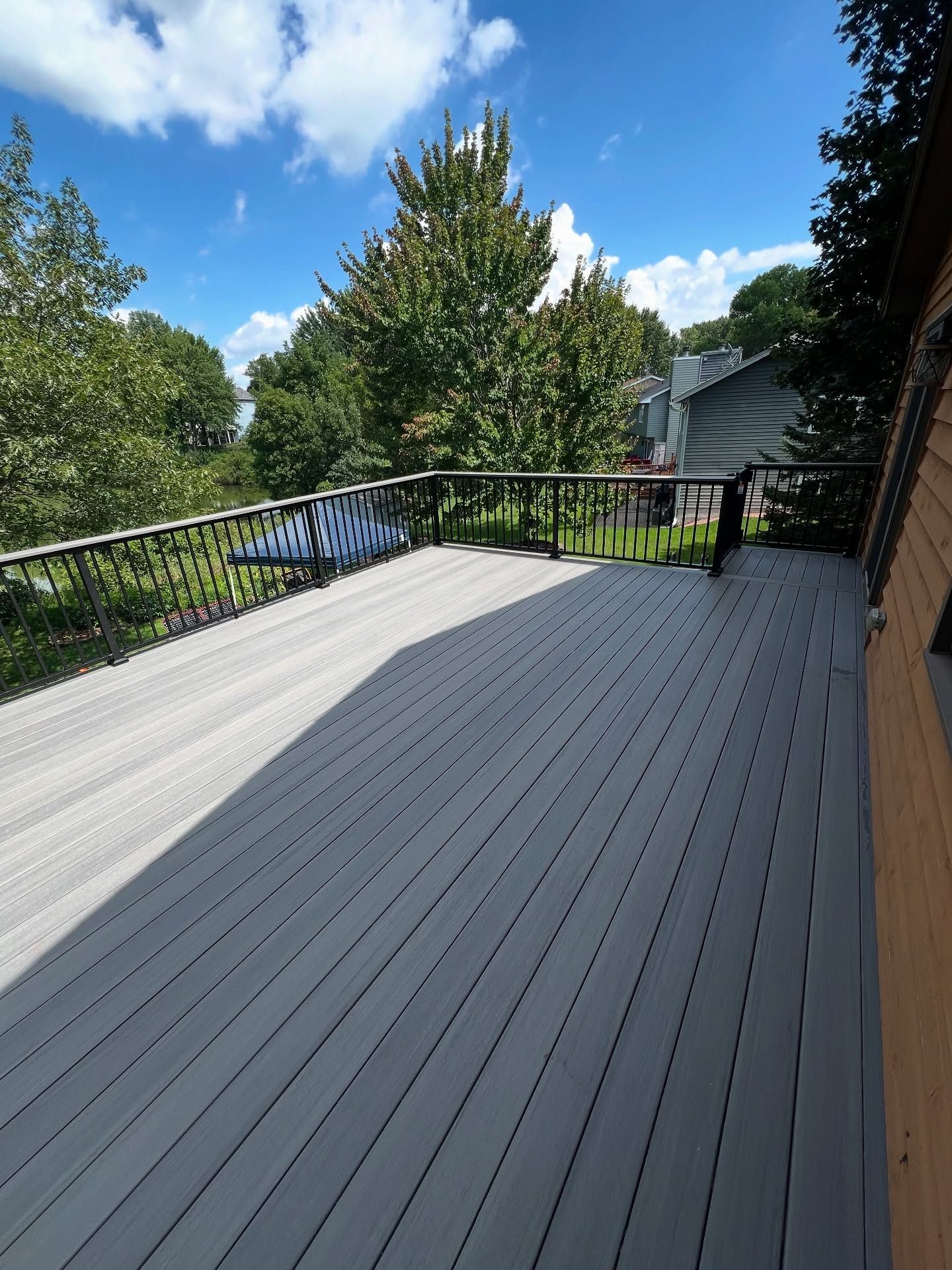 Gray deck with black railing overlooking trees and a blue sky.