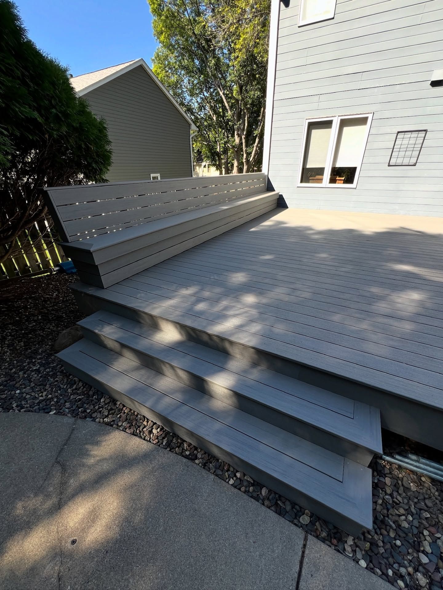 Gray composite deck with steps leading down to a paved area, attached to a gray house.