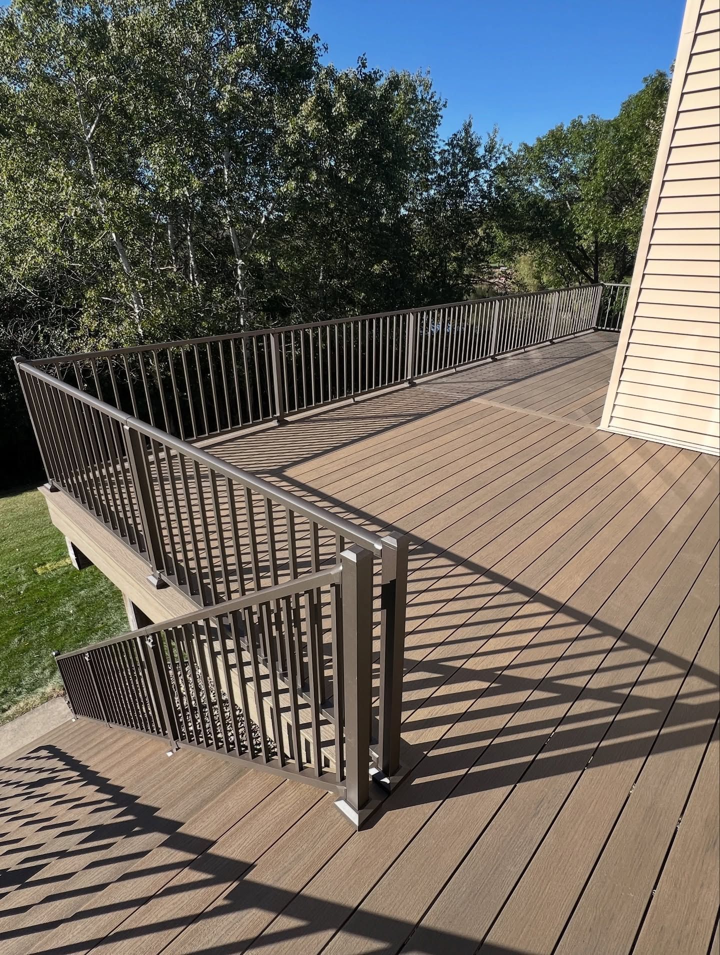 Brown composite deck with metal railings. Sunny day with shadows from trees.