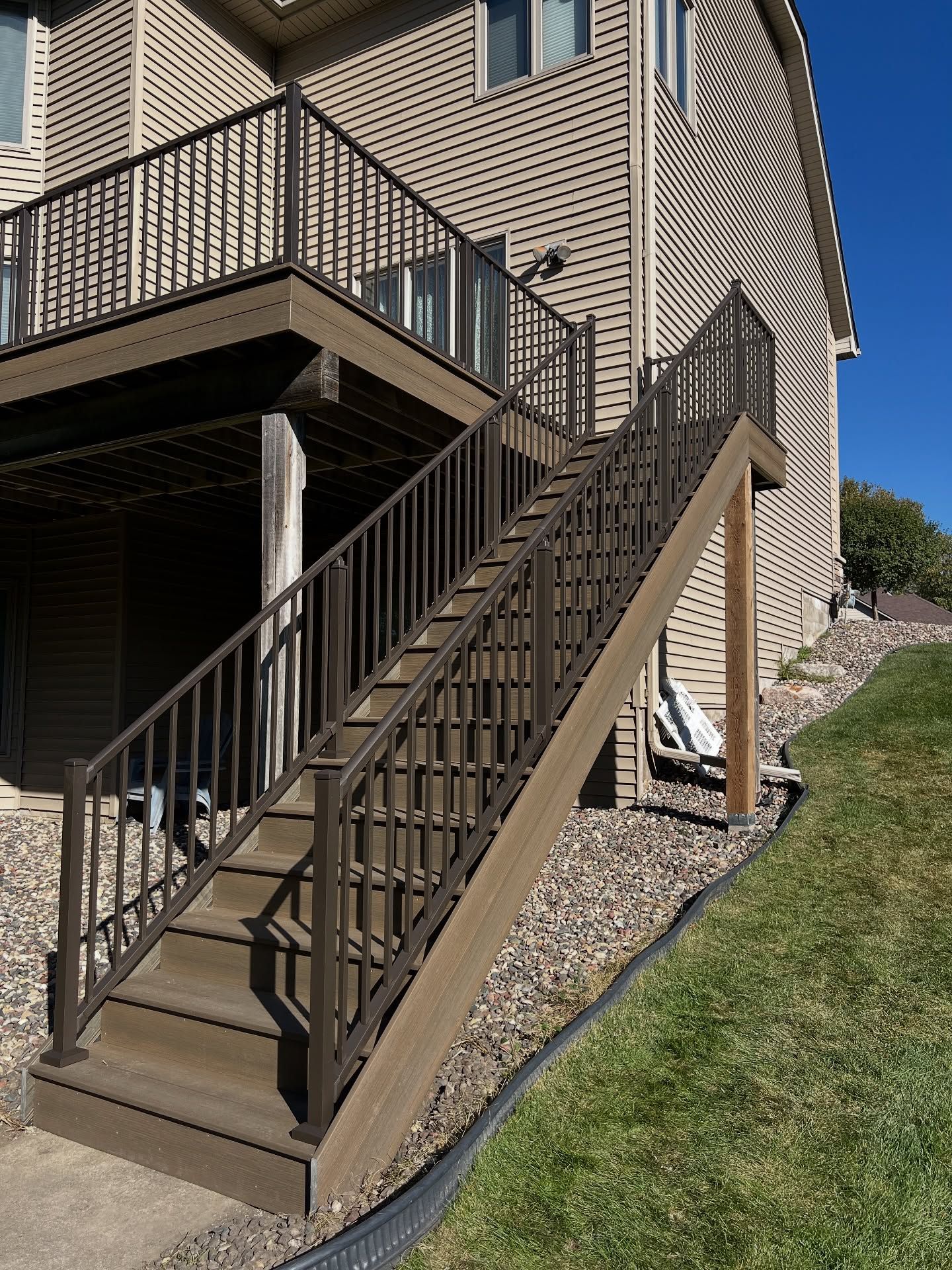 Outdoor staircase with brown railings leading up to a deck attached to a light-colored building.