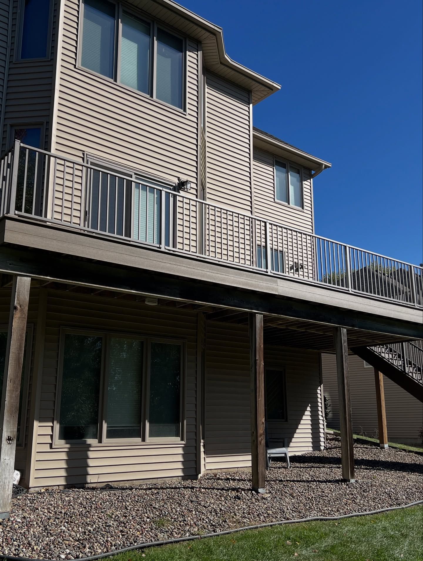 Two-story house with wooden deck, tan siding, and blue sky.