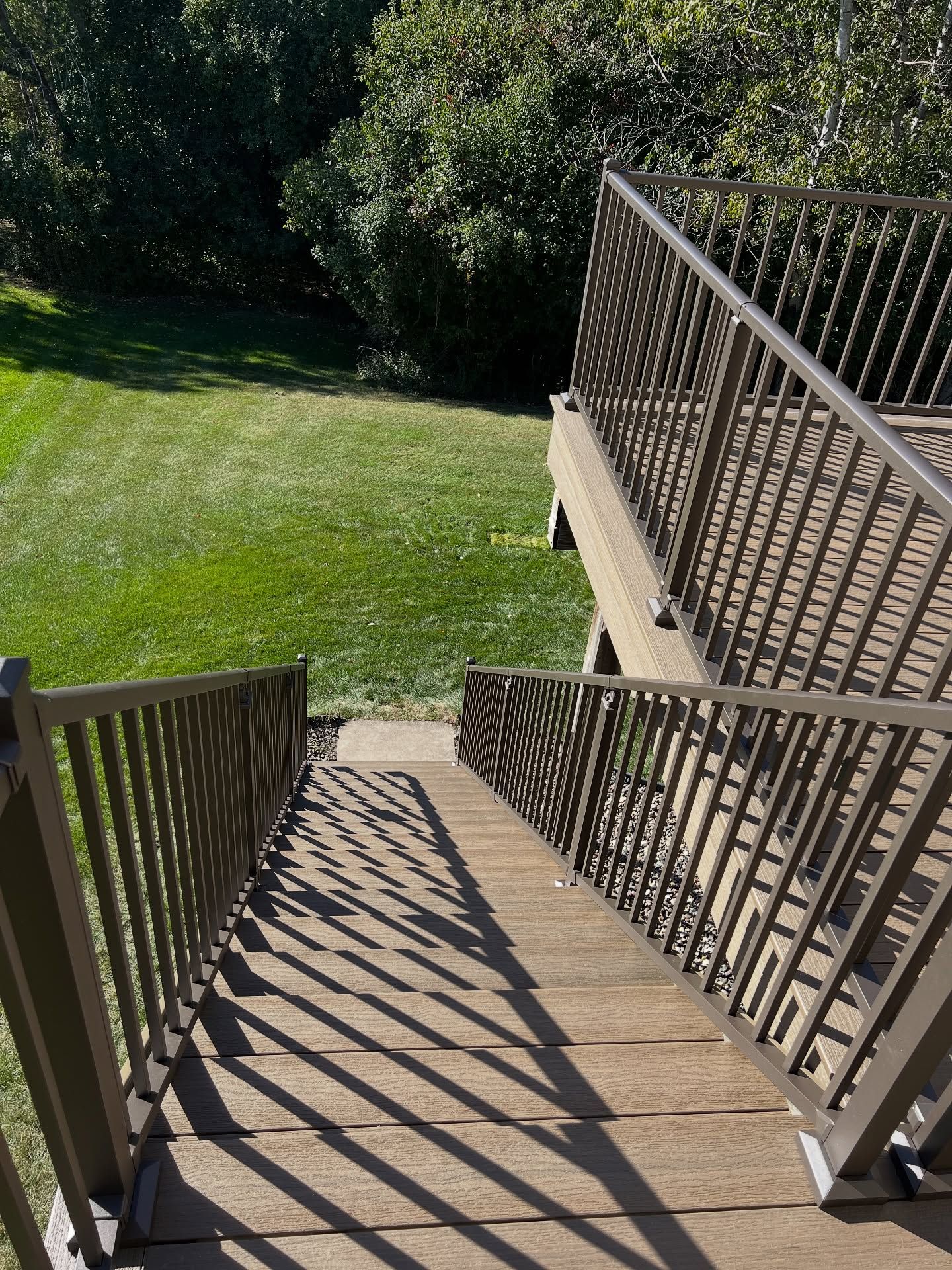 Wooden deck with brown railings and steps leading to a grassy yard.