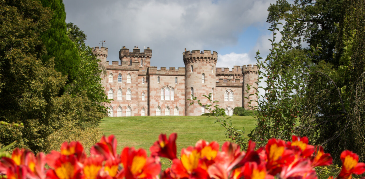 A castle is surrounded by trees and flowers in the foreground. National trust work