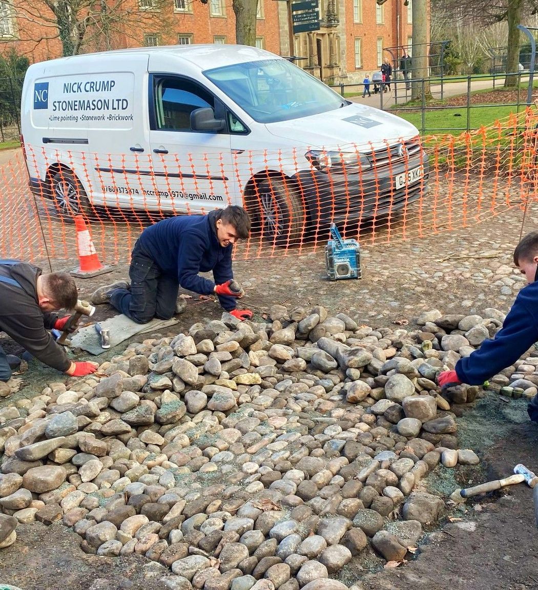 A group of people are working on a cobblestones rocky area in front of a van.
