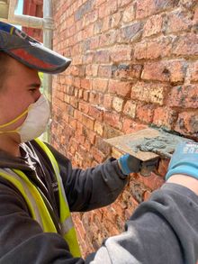 A man wearing a mask and gloves is working on a brick wall.