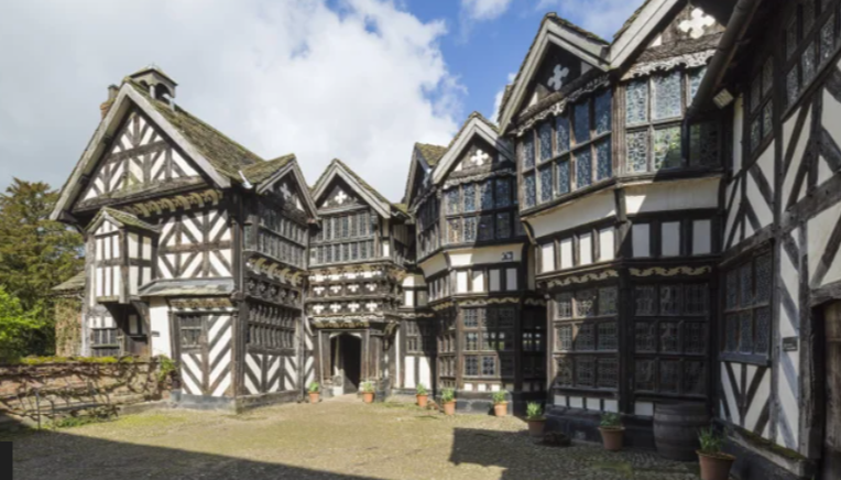 A large black and white house with a lot of windows is surrounded by trees. National trust work