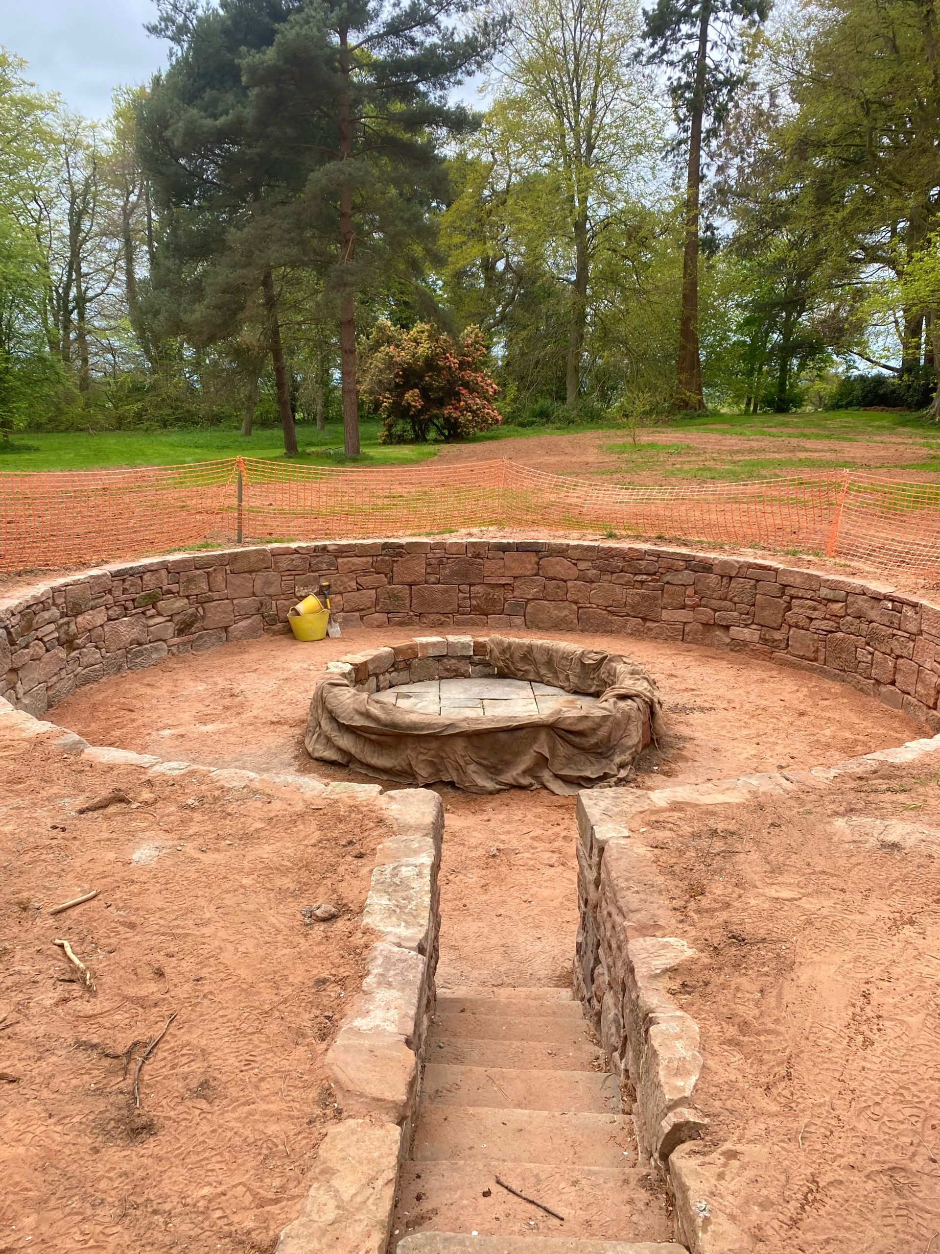 A stonewalled  pit in the middle of a dirt field with trees in the background. . Stonemasons Cheshire