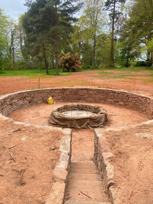 A stonewalled pit in the middle of a dirt field with trees in the background. . Stonemasons Cheshire
