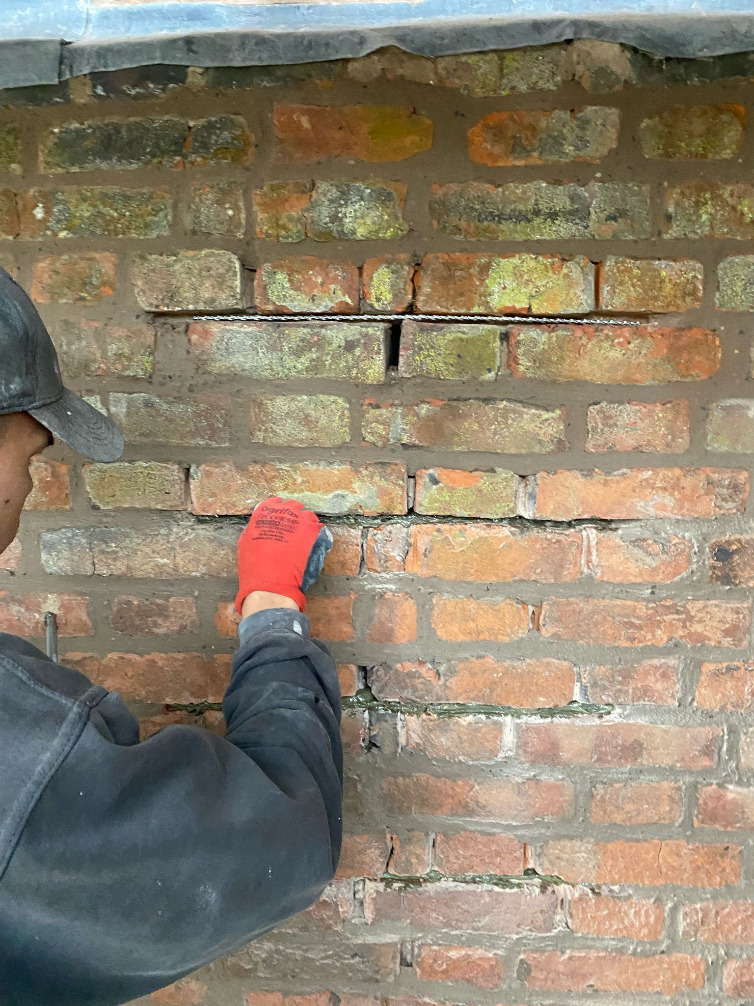A man wearing red gloves is working on a brick wall.
