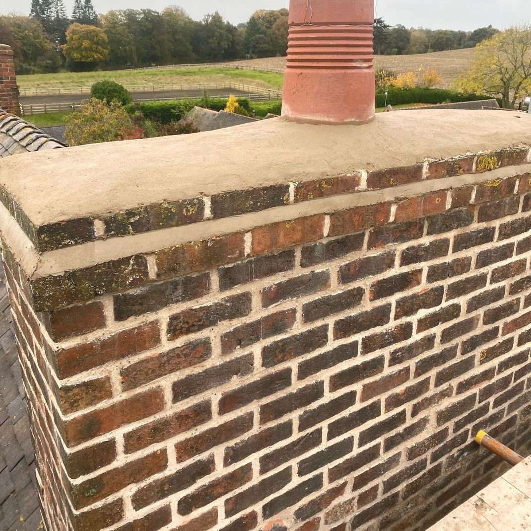 A brick chimney on top of a roof with trees in the background
