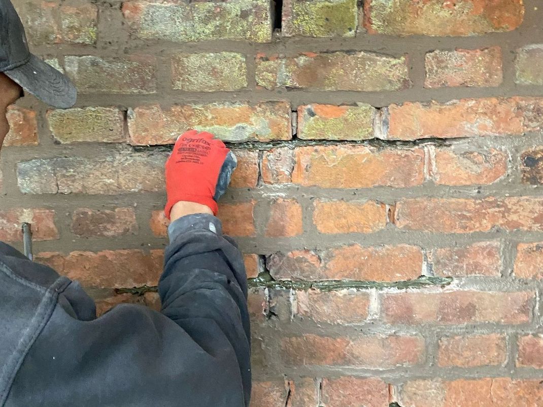 A person wearing red gloves is working on a brick wall.