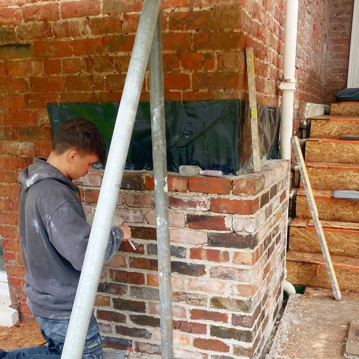 A man is repointing a brick wall next to stairs
