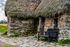 A stone building with a thatched roof and a bench in front of it.