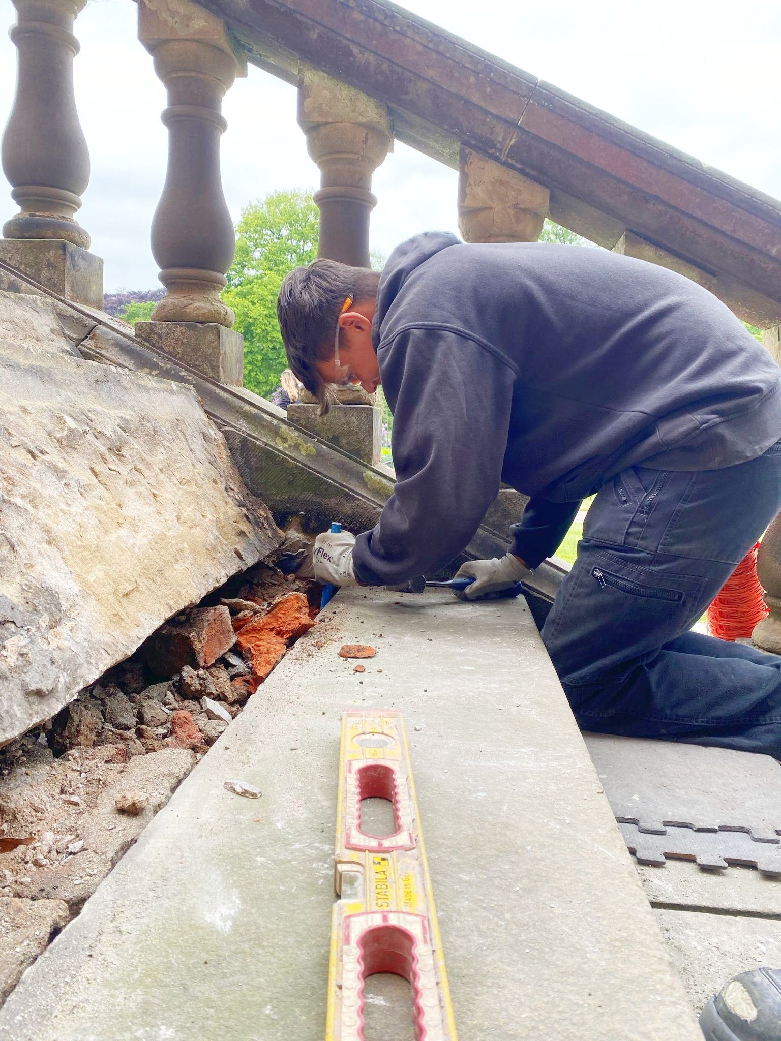 A man is kneeling down on the ground next to repair stone steps